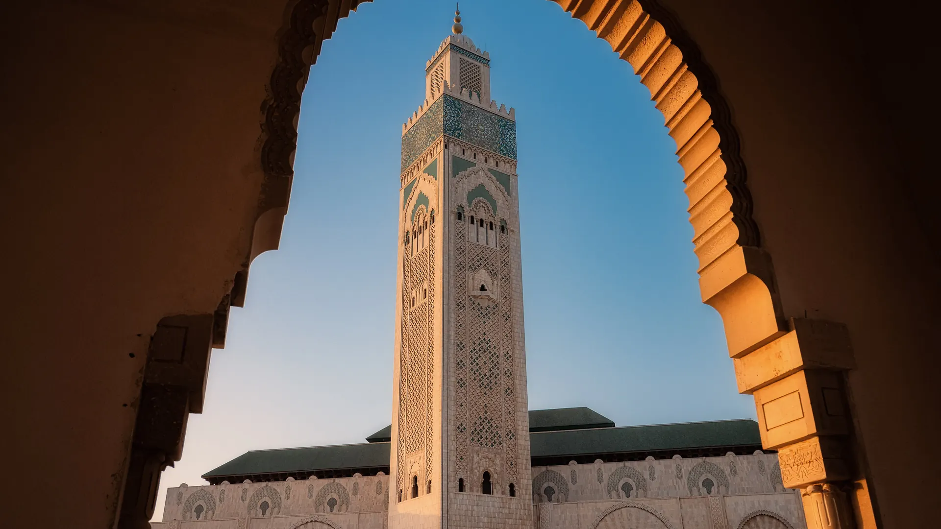 Minaret of the Hassan II Mosque in Casablanca framed by a carved archway in golden light